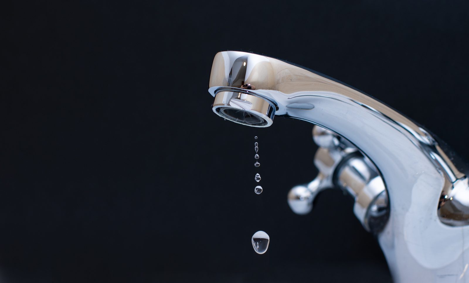 Chrome faucet dripping water drops against a dark background